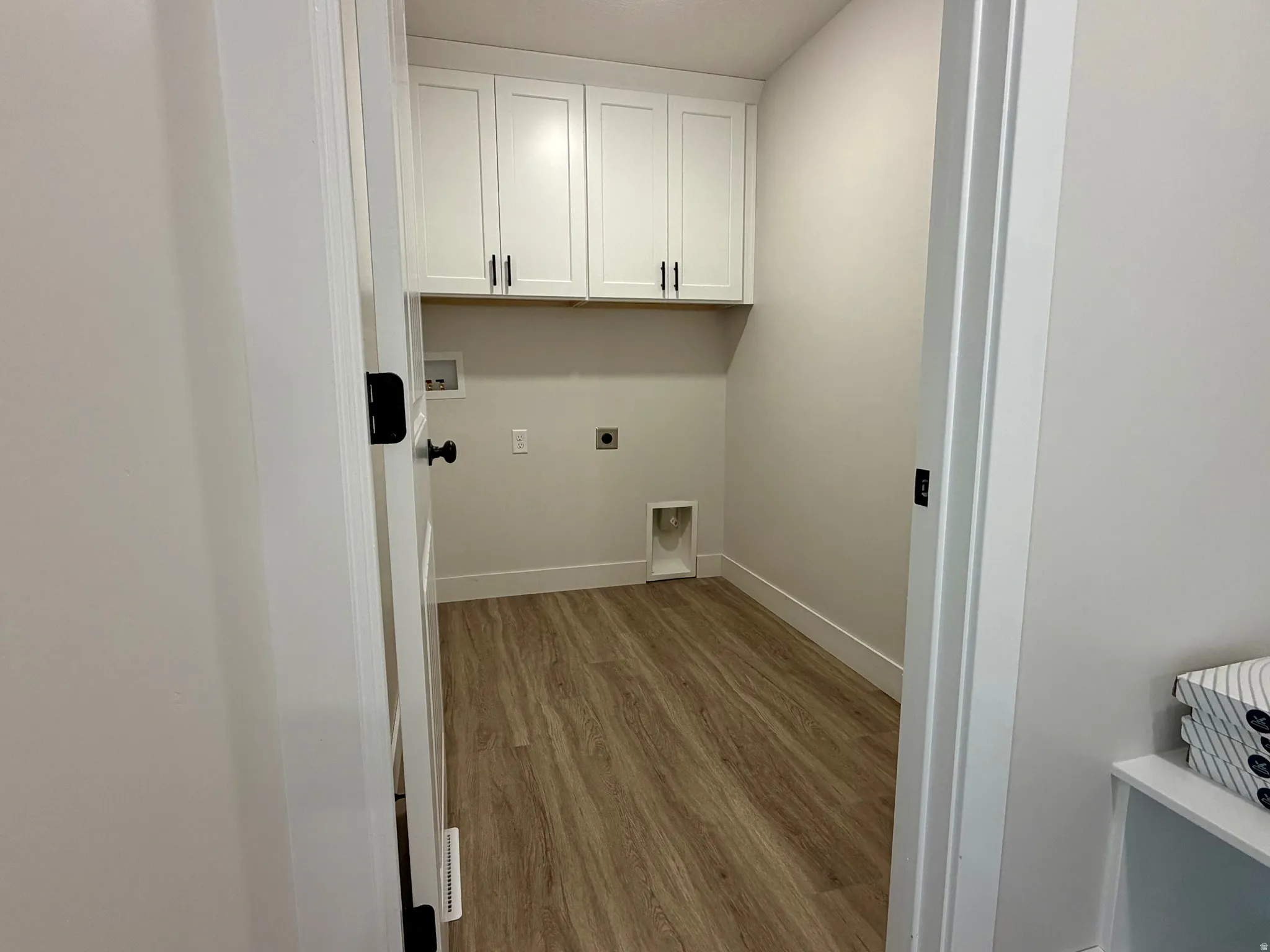 Laundry room featuring white shaker-style cabinetry with matte black hardware, wood-finish flooring, and light-toned walls