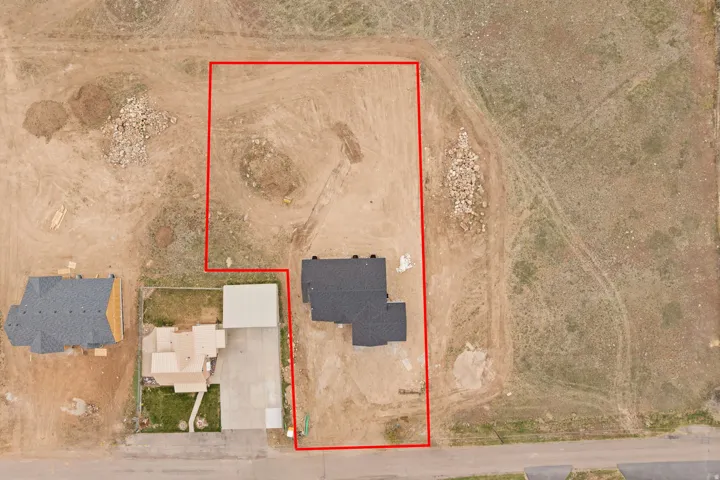Spacious undeveloped land parcel outlined in red, featuring a partial residential structure with a dark shingle roof