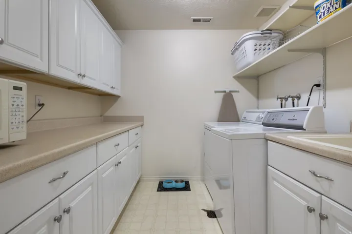 Dedicated laundry space featuring white cabinetry, light-toned countertops, and open shelving