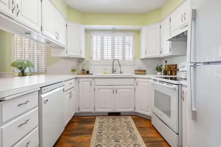 Bright kitchen featuring white cabinetry, white appliances, and wood-finish flooring