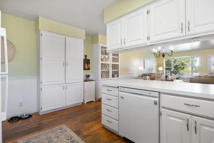 Kitchen featuring white cabinetry, wood-finish flooring, integrated dishwasher, and a built-in pantry cabinet