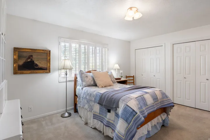 Primary bedroom featuring a window with white plantation shutters, two bi-fold closet doors, and a ceiling-mounted light fixture
