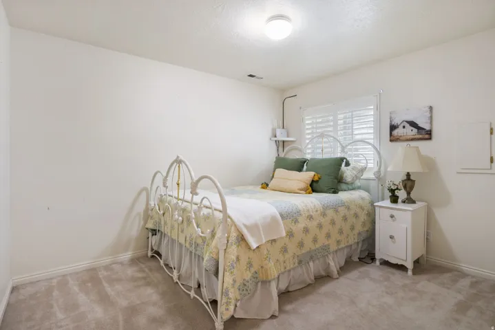 Basement bedroom featuring a window with white plantation shutters, white baseboards, and a flush-mount ceiling light fixture
