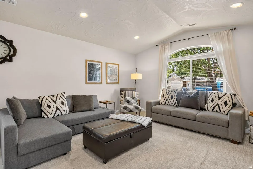 Spacious living area featuring light-toned carpeting and a vaulted ceiling with recessed lighting