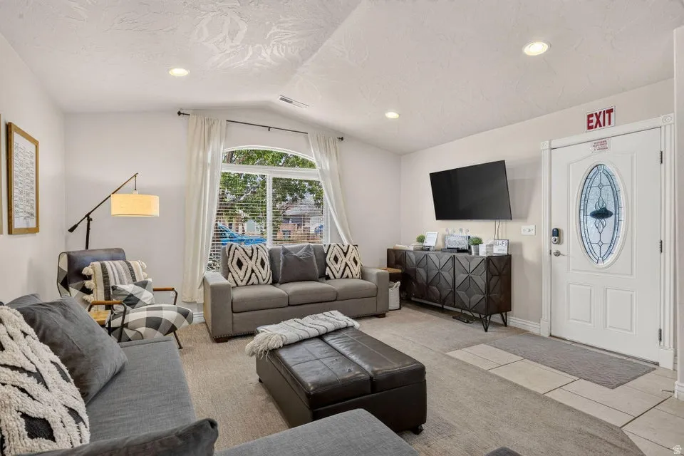 Spacious living area featuring an arched window, recessed lighting, carpet flooring, and a white entry door with an oval-shaped stained glass insert