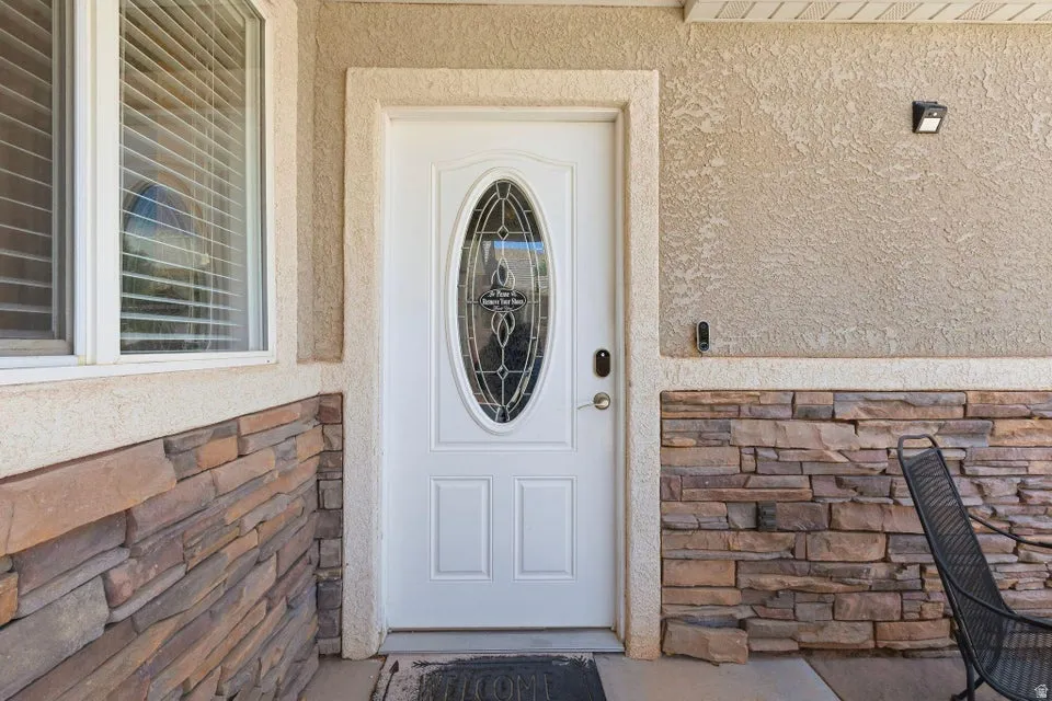Entryway featuring a white door with an oval decorative glass insert, textured stucco siding, and stone veneer accents