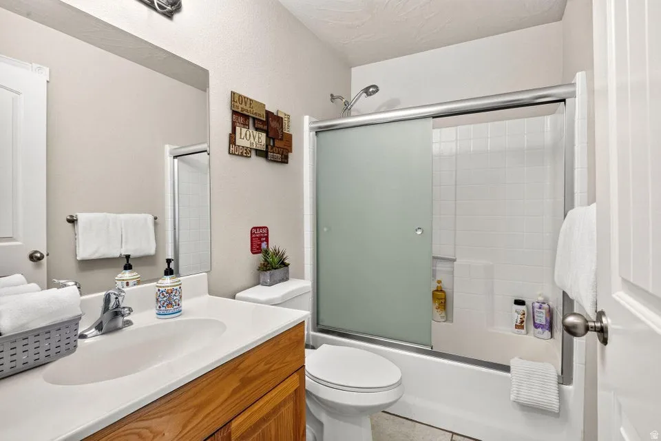 Bathroom featuring a shower-tub combination with sliding frosted glass doors, white subway tile surround, and an integrated shelf