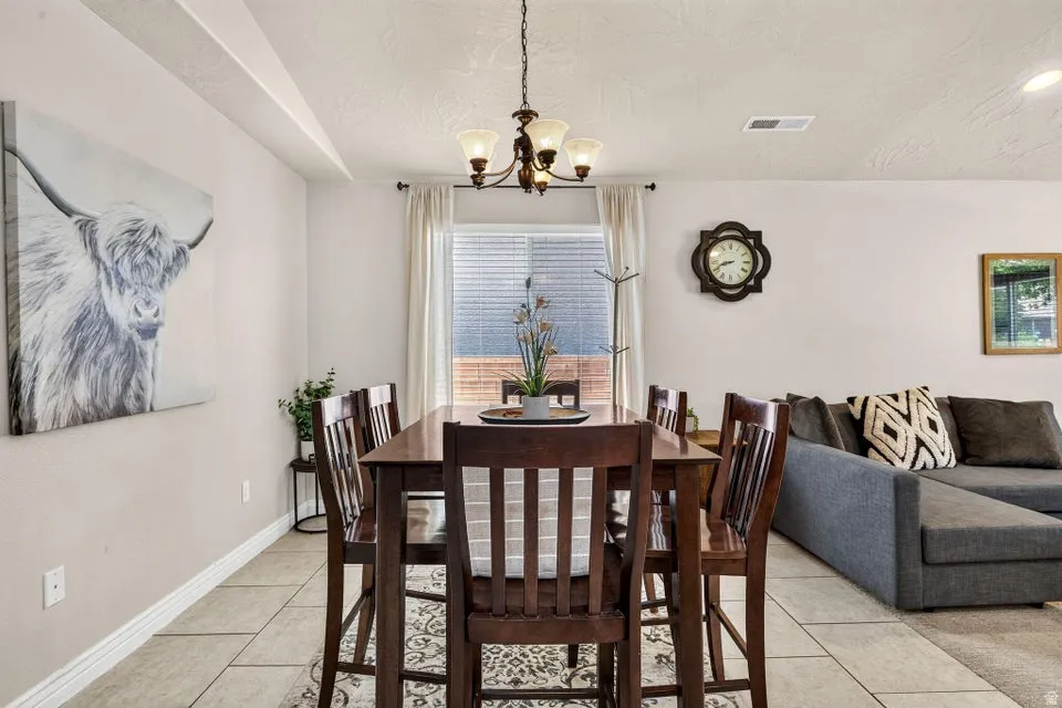 Open-concept dining area featuring a dark wood-finish dining table with matching chairs, an overhead chandelier, and tile flooring
