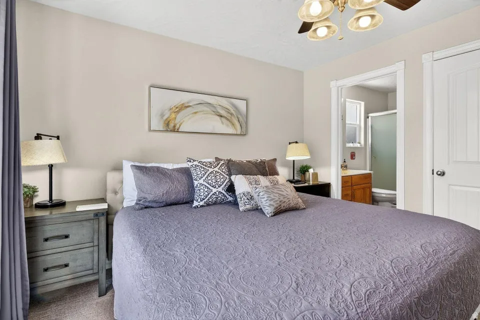 Bedroom featuring a light gray upholstered headboard, ceiling fan with integrated lighting, and a white paneled door