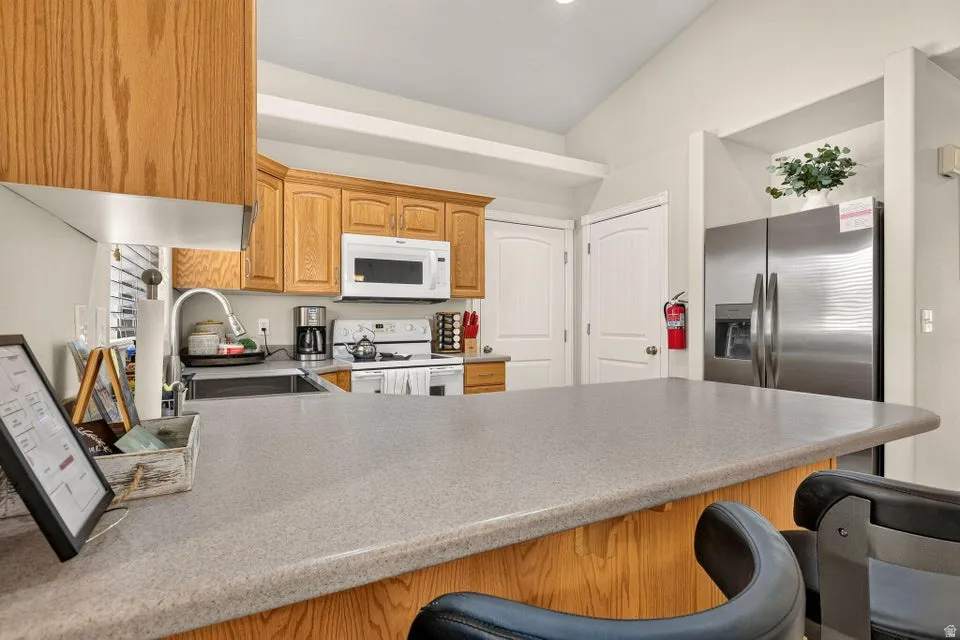 Kitchen featuring light wood cabinetry, a large kitchen island with counter seating, stainless steel refrigerator, white over-range microwave, and a stainless steel sink with a high-arc faucet