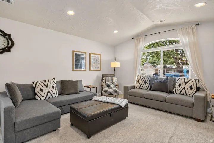 Spacious living area featuring light-toned carpeting and a vaulted ceiling with recessed lighting