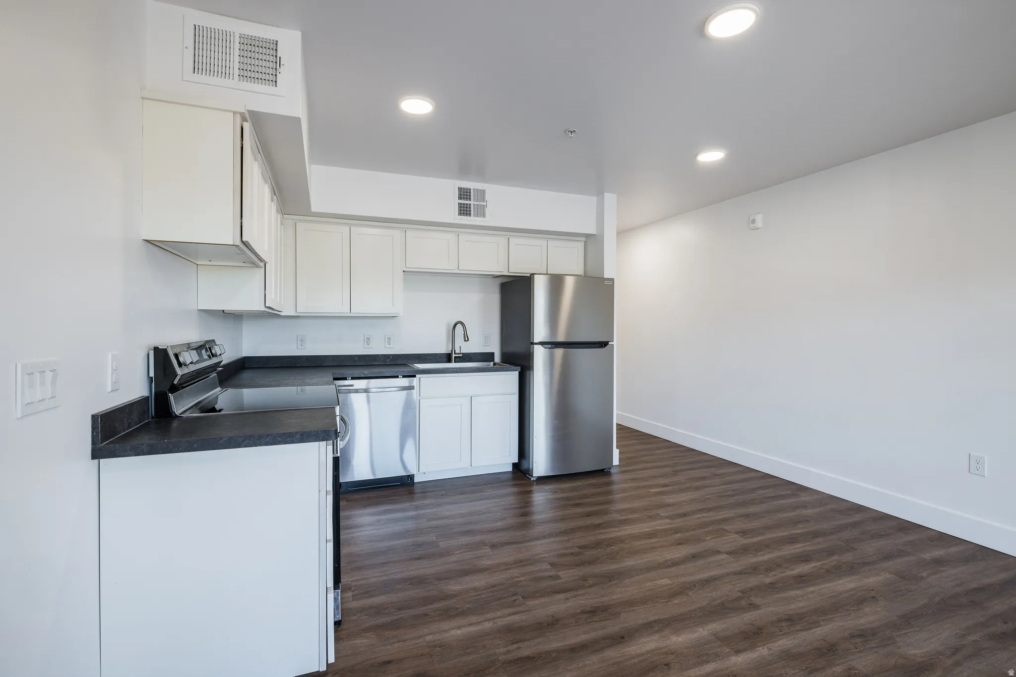 Contemporary kitchen featuring white cabinetry, dark countertops, stainless steel appliances, and wood-finish flooring