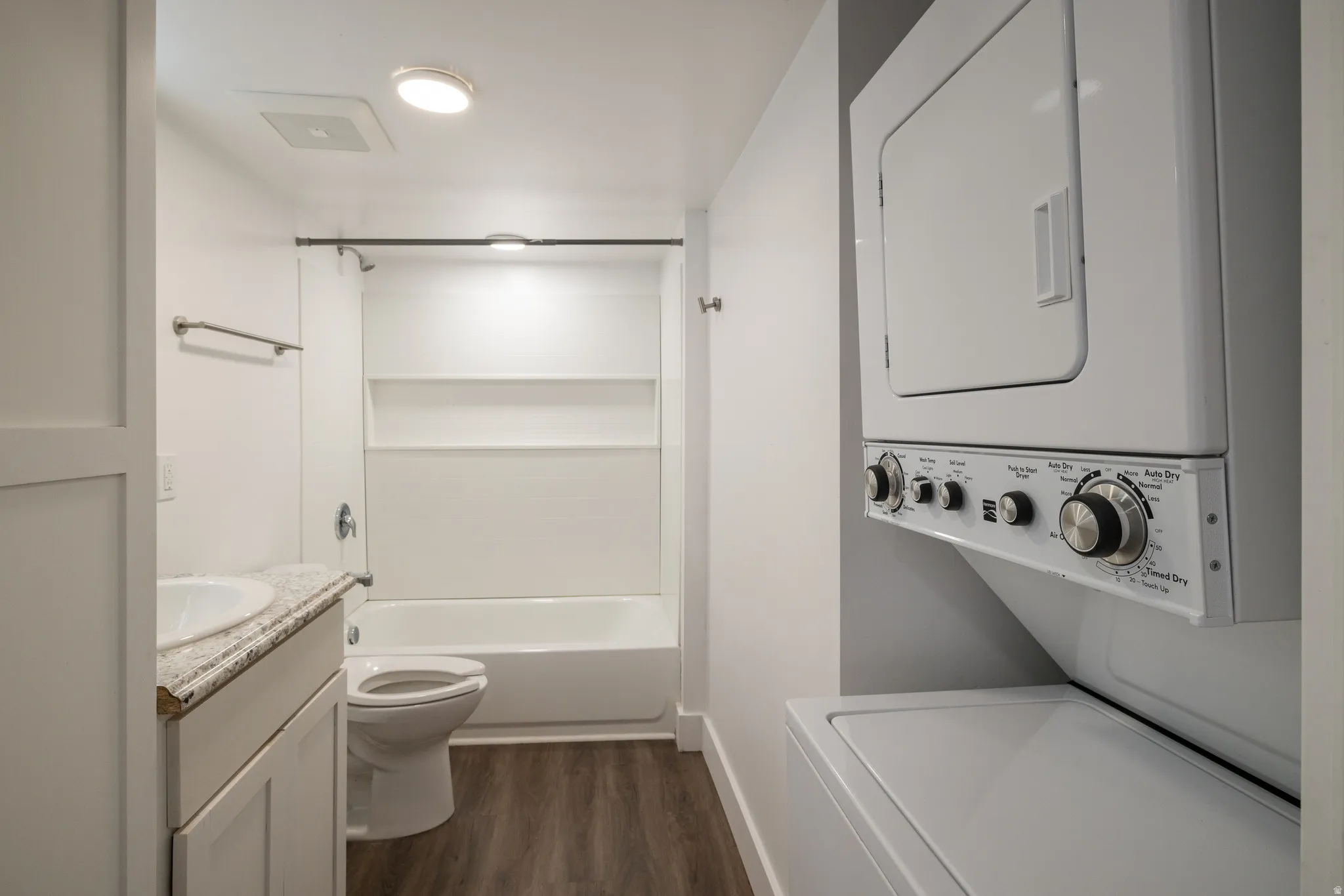 Bathroom featuring wood-finish flooring, a white vanity with an undermount sink, a shower-over-tub combination, and a stacked washer and dryer unit