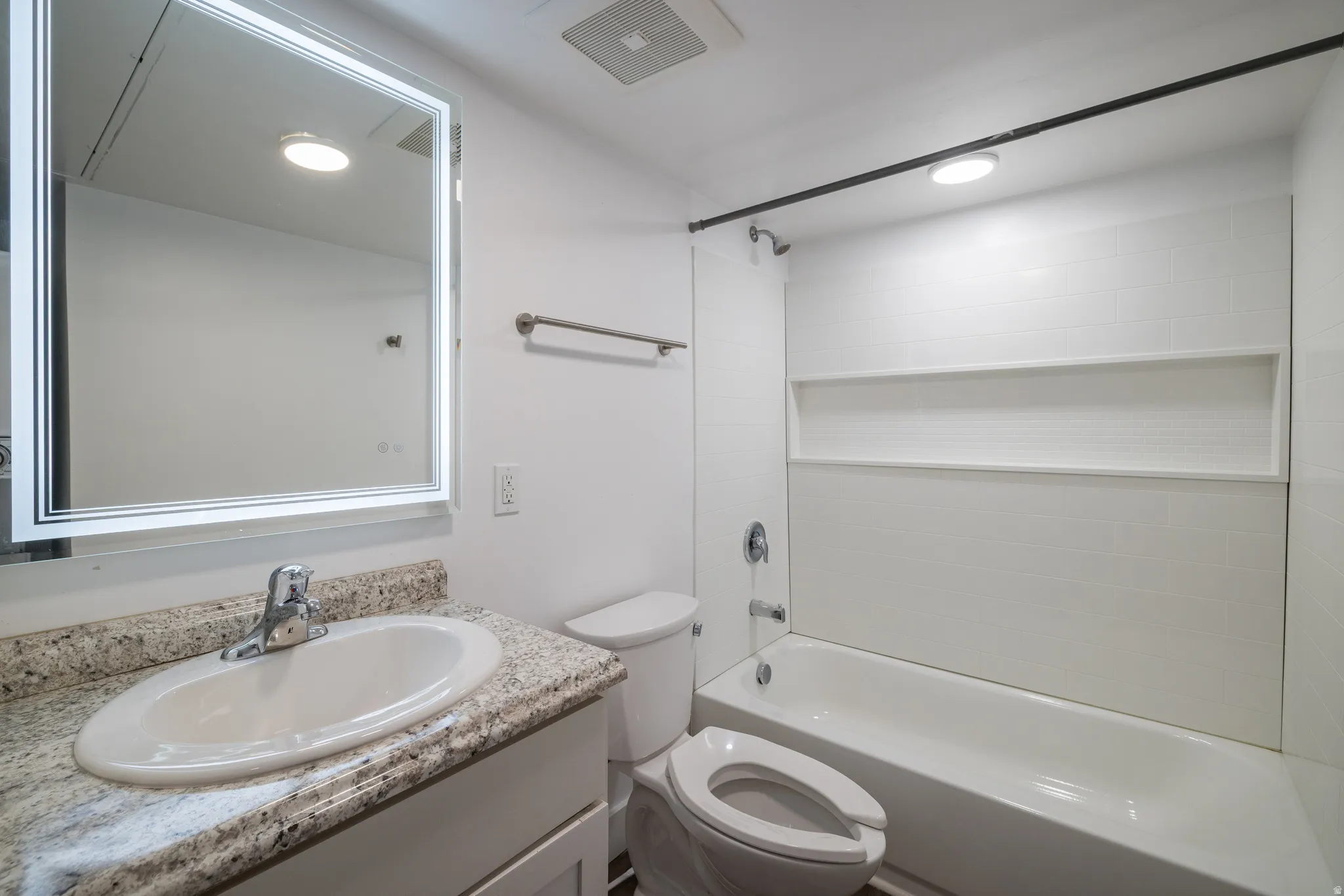Bathroom featuring a full vanity with an integrated sink, stone-finish countertop, and a lighted mirror