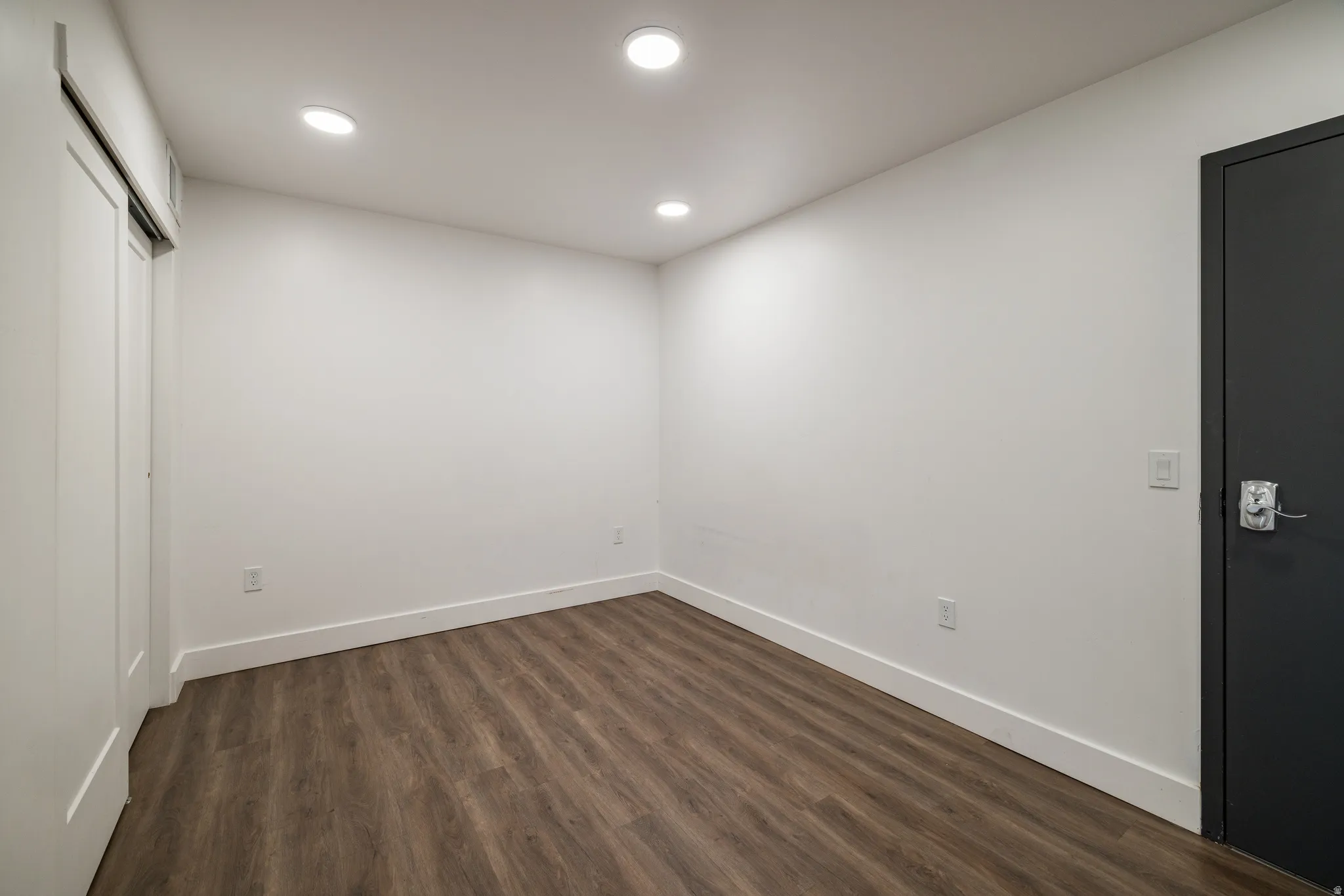 Spacious room featuring wood-finish flooring, recessed lighting, white baseboards, and a sliding barn-style closet door