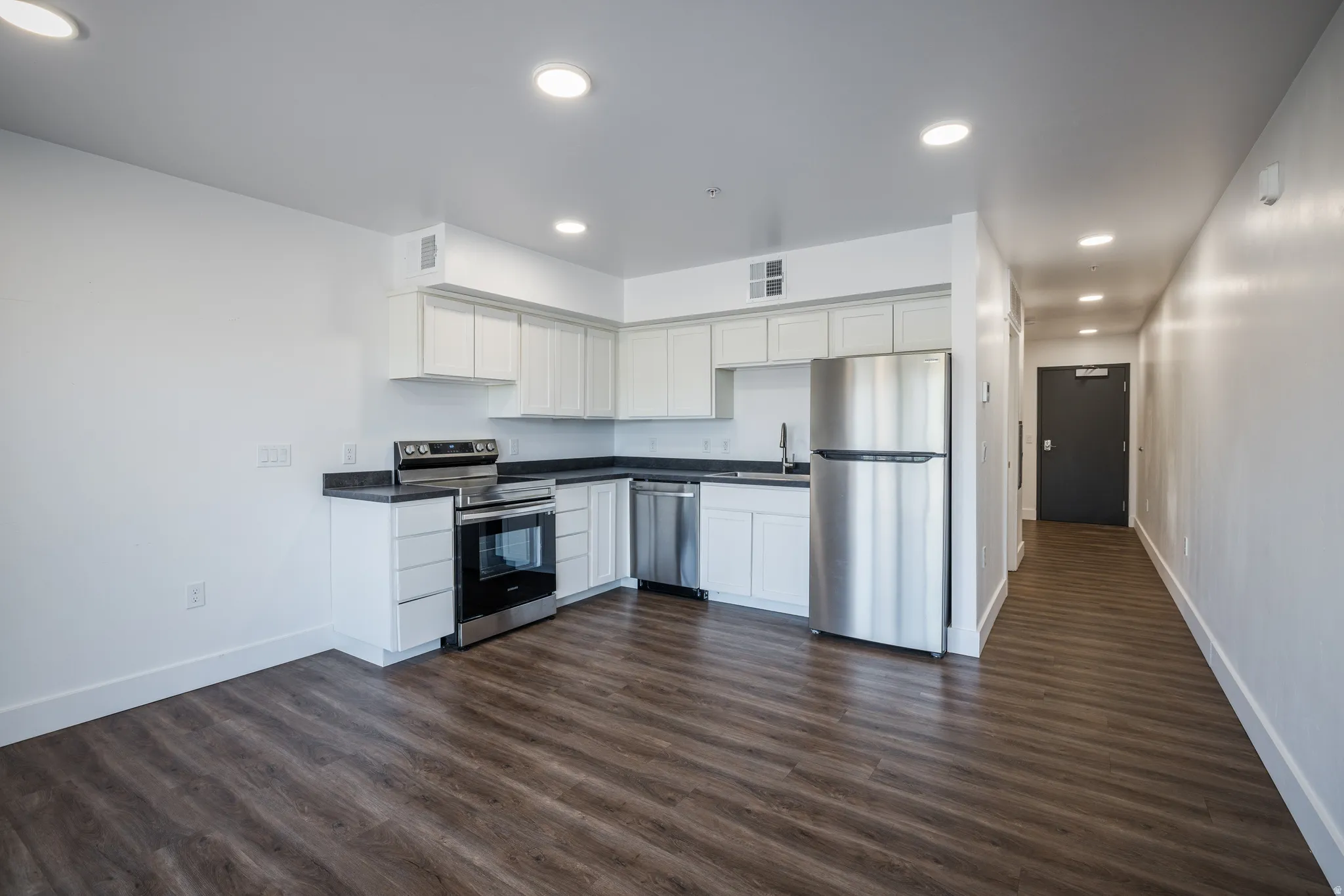 Open-concept kitchen featuring white cabinetry, dark countertops, stainless steel appliances, and wood-finish flooring