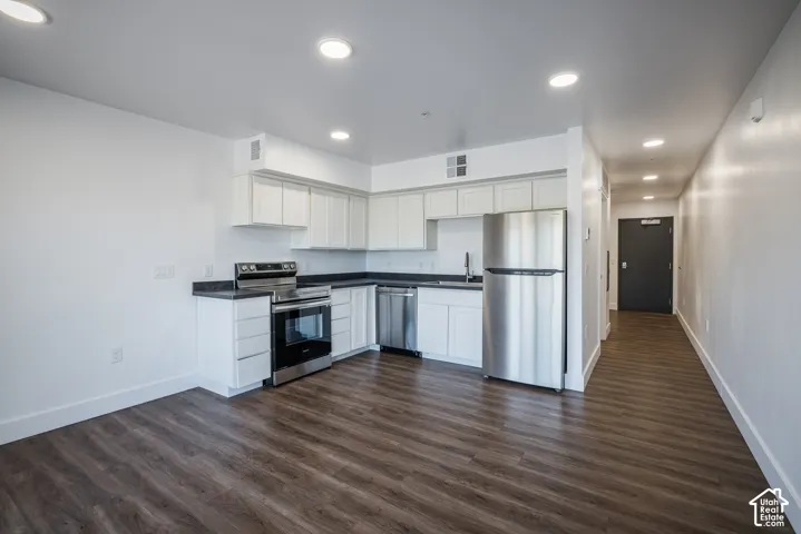 Open-concept kitchen featuring white cabinetry, dark countertops, stainless steel appliances, and wood-finish flooring
