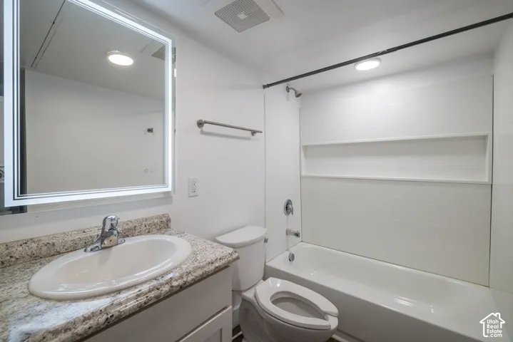 Bathroom featuring a full vanity with an integrated sink, stone-finish countertop, and a lighted mirror