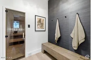 Glass-door sauna with wood interior, light-toned wood flooring, textured accent wall, and a built-in wood bench