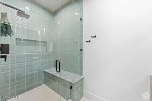 Glass-enclosed shower featuring light green subway tile, a built-in shelf, a bench with a stone surface, and matte black fixtures