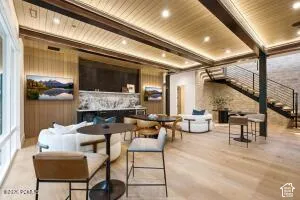 Wood-finish flooring, recessed lighting, exposed ceiling beams, built-in wet bar with stone countertop, and open-tread staircase with metal railings