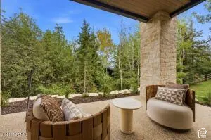 Covered patio with stone column, concrete flooring, and surrounding mature trees