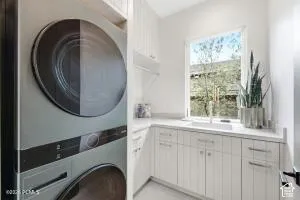 Stacked laundry appliances, white cabinetry with silver-tone hardware, white countertop, and a single window