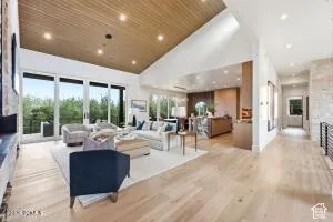 Vaulted ceiling with wood-finish planks, large format window wall, light wood-finish flooring, recessed lighting, and stone veneer wall