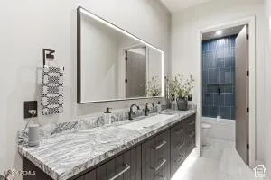 Double vanity with a stone countertop, under-cabinet lighting, and a large illuminated mirror