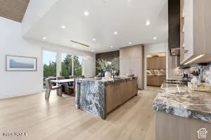 Spacious kitchen and dining area featuring wood-finish flooring, a large island with a substantial countertop, extensive cabinetry, and recessed lighting