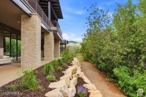Stone-clad exterior columns, multiple balconies with metal railings, sliding glass doors, a stone retaining wall, and a landscaped garden bed