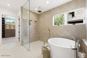 Freestanding soaking tub with floor-mounted faucet, glass-enclosed shower, herringbone-patterned tile wall, recessed lighting, and large wardrobe cabinetry