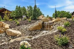 Landscaped water feature with natural rock elements, wood mulch, and varied plantings