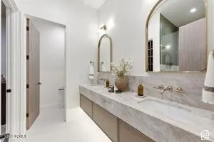 Double vanity featuring integrated sinks and a stone-finish countertop, wall-mounted faucets, and two arched mirrors with brass-finish frames