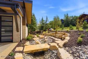 Modern exterior with large windows, natural stone accents, wood-finish eaves, and a landscaped rock garden with stepping stones