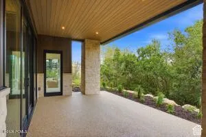 Expansive outdoor patio with a planked wood-finish ceiling, recessed lighting, stone columns, and sliding glass doors