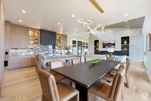 Open-concept dining and kitchen area featuring a black wood-finish dining table, upholstered chairs, wood-finish flooring throughout, recessed ceiling lighting, a modern pendant light fixture, stainless steel appliances, white cabinetry with hardware acce