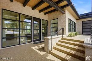 Exterior entry featuring broad stairs, wrought iron railings, an exposed beam ceiling, and expansive windows