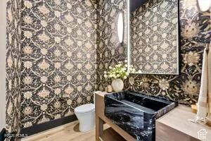 Patterned wall covering, black marble vessel sink, wood-finish flooring, wall-mounted light fixtures, built-in vanity cabinetry