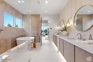 Free-standing soaking tub, dual vanity with undermount sinks, separate glass-enclosed shower, and herringbone-patterned tile accents