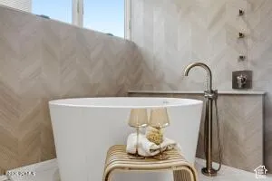 Freestanding soaking tub with a floor-mounted gold-toned faucet, complemented by herringbone-patterned wall tiling and integrated shower controls