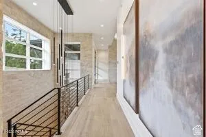 Modern lighting fixture, light wood-finish flooring, white window frames, stone-finish accent wall, and black metal railings