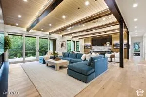 Expansive living area featuring wood-finish flooring, a wood-paneled ceiling with exposed beams, recessed lighting, and large sliding glass doors