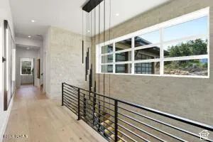 Modern hallway with light wood-finish flooring, linear pendant lighting, and expansive windows framing scenic outdoor vistas