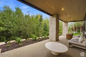 Expansive covered patio featuring a wood-finish ceiling with recessed lighting, stone pillars, and a concrete paver surface