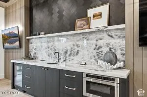 Built-in cabinetry with integrated sink, stone countertop, tile backsplash, and stainless steel microwave