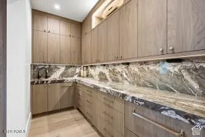 Extensive wood-finish cabinetry, under-cabinet lighting, L-shaped countertop, integrated sink, and wood-finish flooring