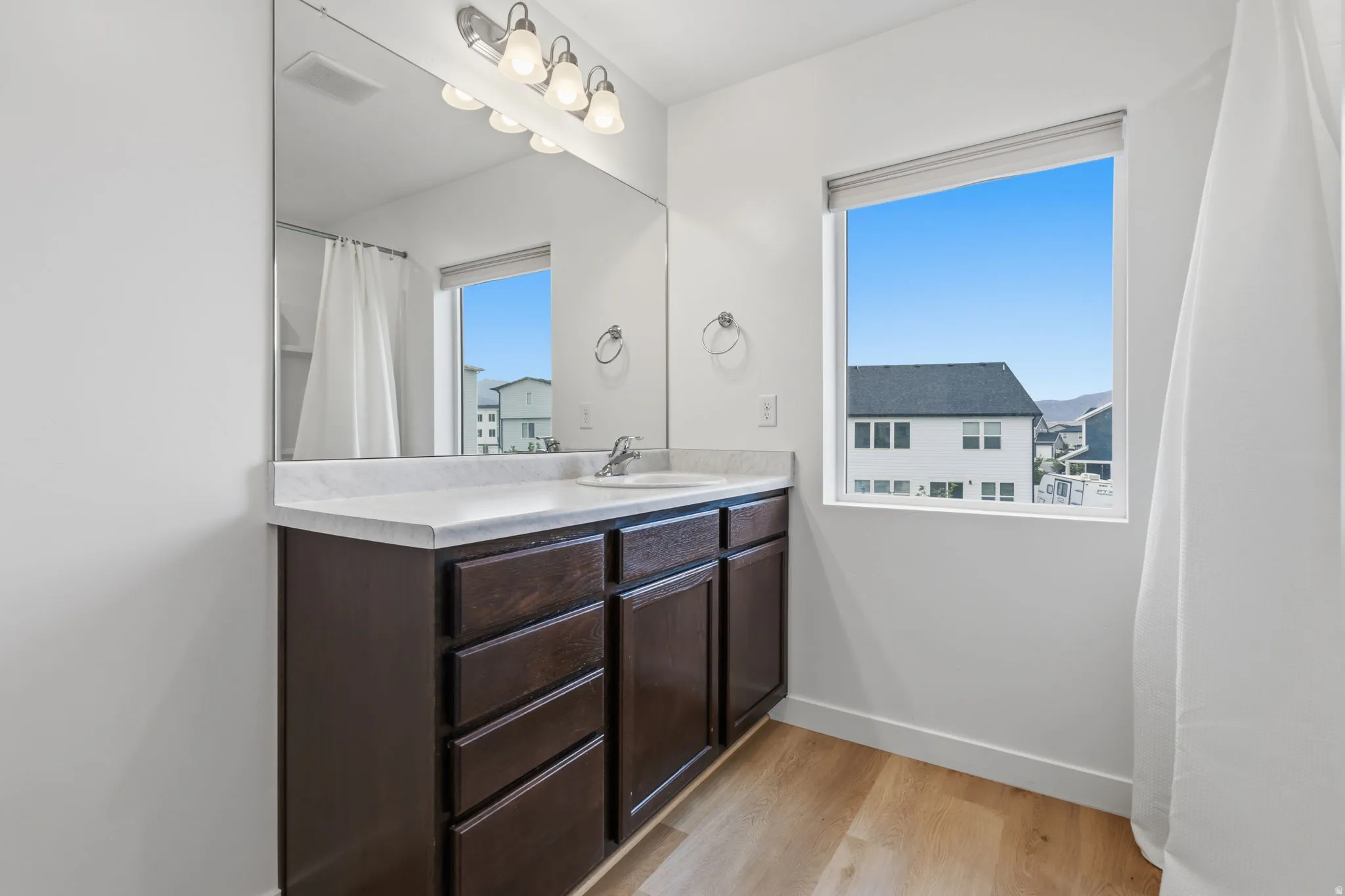 Bathroom featuring a dark wood-finish vanity with a white countertop, chrome faucet, and a large mirror with integrated lighting