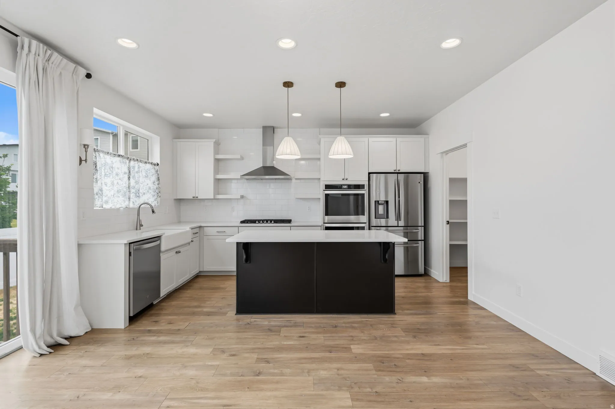 Modern kitchen featuring a black island with a white countertop, stainless steel appliances, white cabinetry, and wood-finish flooring