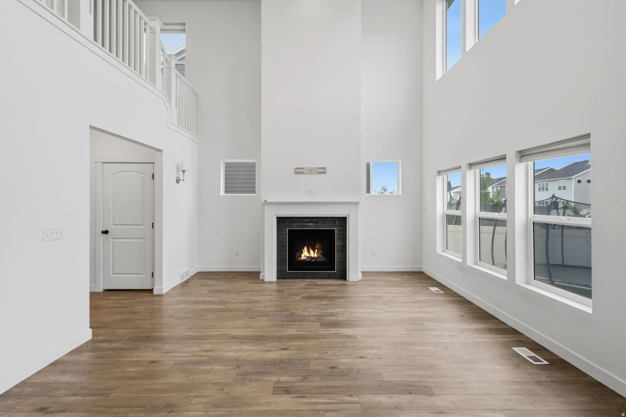 Two-story living area featuring wood-finish flooring, a contemporary fireplace with a dark tile surround and white mantel, and multiple windows including upper transom windows